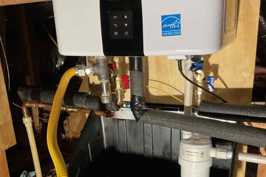 New energy-efficient tankless water heater installed in a home attic with a protective drain pan and properly routed and secured piping.
