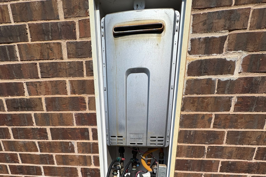 Older tankless water heater mounted on the outside of a homes, showing signs of wear and in need of maintenace.