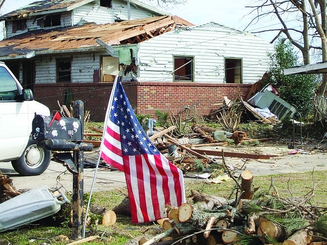 English: A U.S. flag stands outside a damaged ...