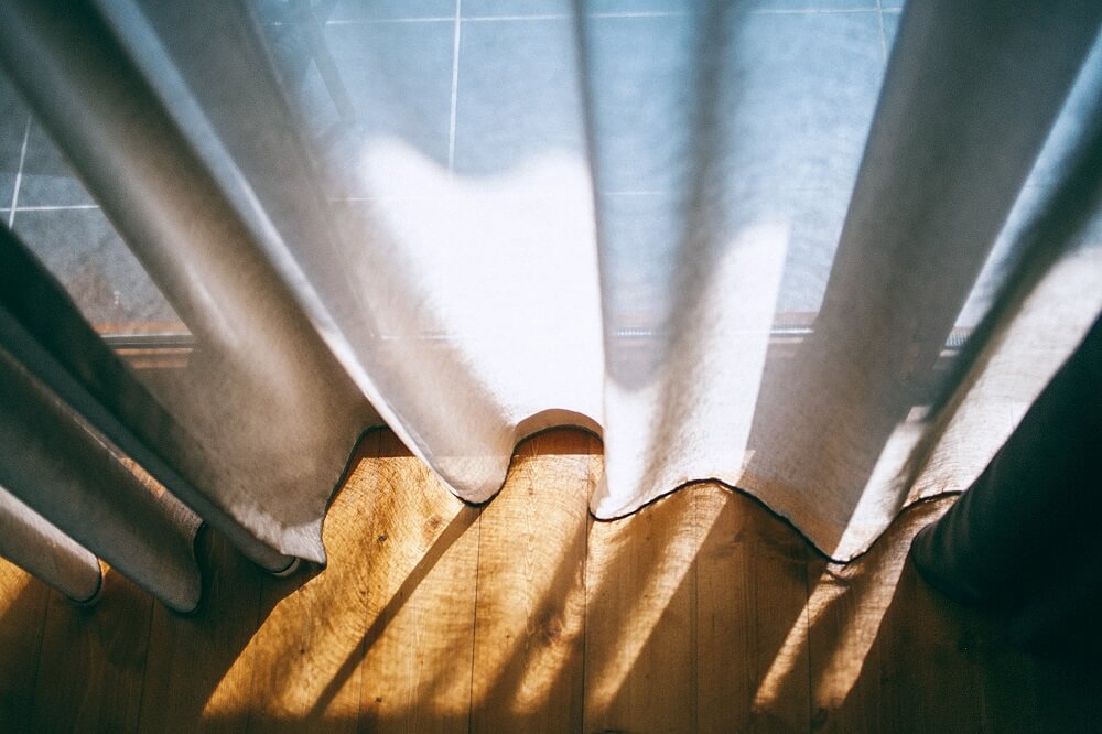 sun shins through white curtains onto hardwood floor